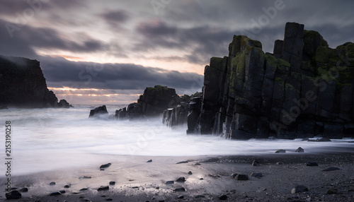 Dramatic rocky beach with dark cliffs at sunset