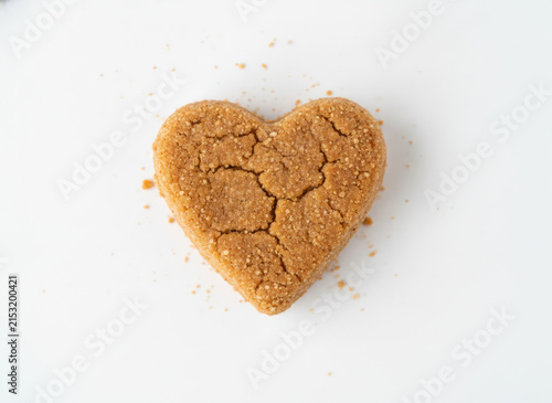 Heart-shaped gingerbread cookie with cracks on a white background, top view, concept of love and homemade treats