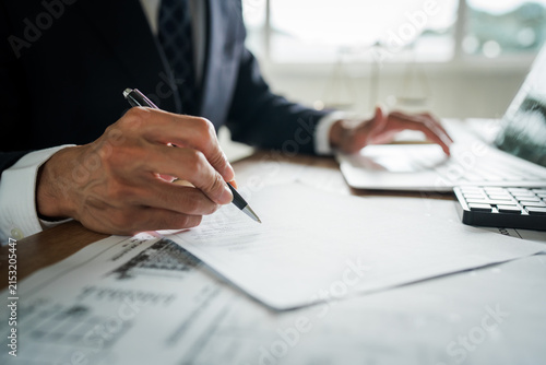 Real estate professional reviewing property documents at a desk with a house model, legal gavel, architectural plans, laptop, and scales, representing property law and transactions.