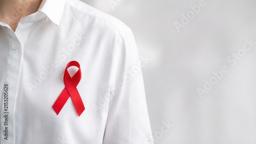 Red awareness ribbon pinned to a white shirt chest, symbolizing HIV/AIDS and health awareness support