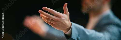 Closeup of a conductor hand extended with open palm for orchestral concert poster and music event banner design with shallow depth of field