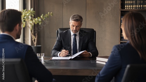 Male executive in a suit reviewing and signing documents at a conference table during a formal client meeting in a modern office
