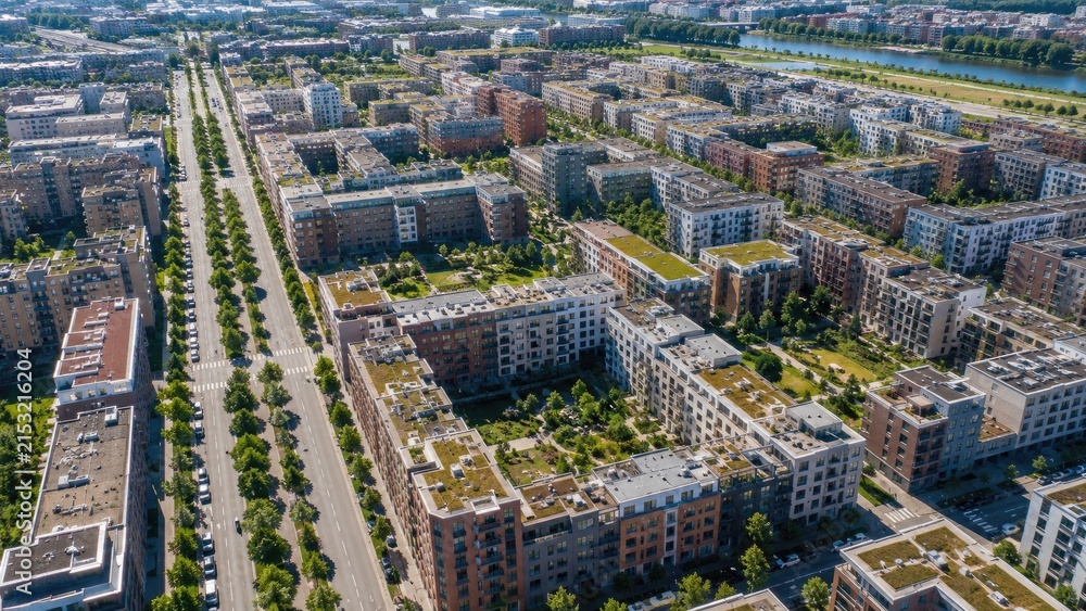 Fototapeta premium Aerial view of a modern residential neighborhood with apartment blocks, green roofs, courtyards and a tree-lined boulevard
