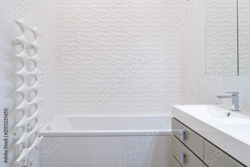 Modern white bathroom with bathtub, textured wall and minimalist vanity