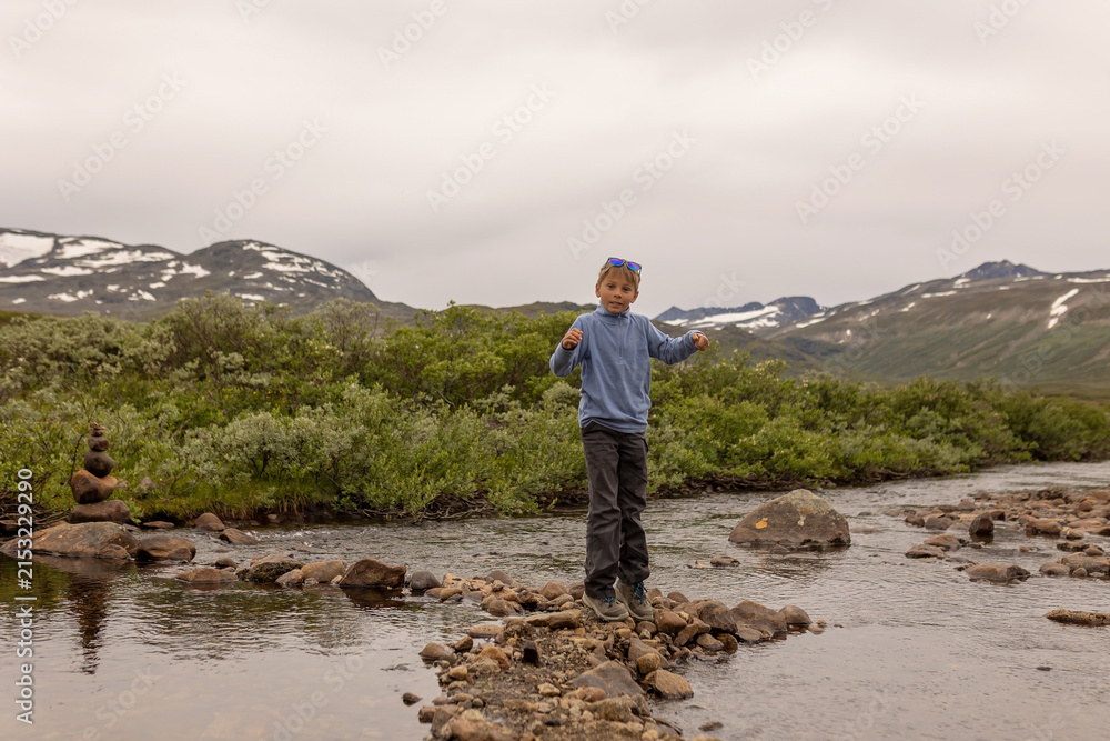Fototapeta premium Beautiful european family with children and pet dog hiking Knutshoe summit with blue lake in mountain landscape in Jotunheimen National Park in Norway, mountains of Besseggen in background, cloudy sky