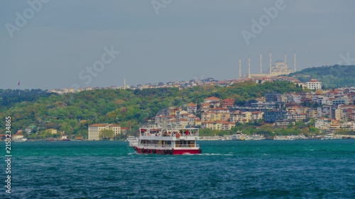 Scenic view of a passenger ferry sailing across the blue waters of the Bosphorus in Istanbul featuring a hillside city and historic mosque under a clear sky in Turkey