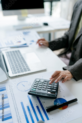 Professional working hands engaging with a calculator and reviewing various financial documents. Including charts and graphs. On a modern office desk