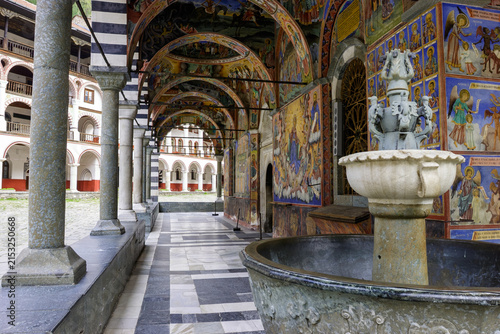 Фотография The Rila Monastery in Bulgaria, a UNESCO World Heritage site, features stunning frescoes adorning its cloister walkways, with a fountain in the foreground