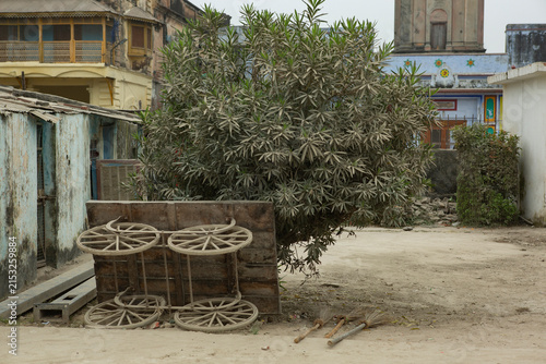 Old wooden cart with wheels resting against a bush in an Indian street