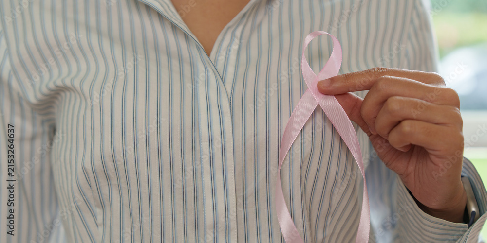 © Natee Meepian - Person holding pink ribbon on striped shirt for breast cancer awareness campaign © Natee Meepian - Person holding pink ribbon on striped shirt for breast cancer awareness campaign