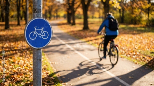 Round blue bicycle lane sign standing beside a person riding a bicycle during golden autumn