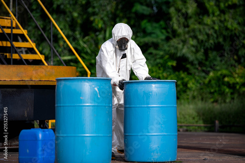 Workers in protective suits handle blue chemical barrels during hazardous material safety training