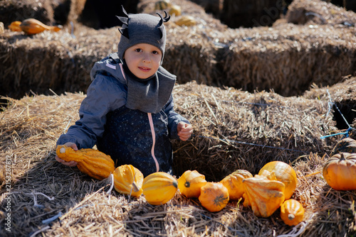 Cute kid having fun at a pumpkin farm with hay stacks. 