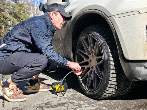 Man inflating car tire with portable air compressor. Vehicle maintenance and roadside repair concept for automotive service and travel safety.