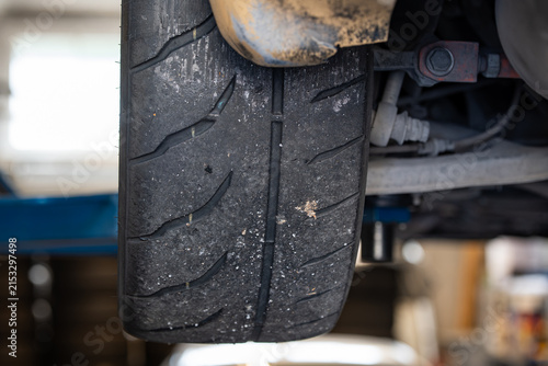 Foto Close up view of worn tread rubber and pick-up debris on a wide semi-slick rear motorsport tire on a raised vehicle