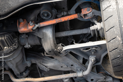 Obraz na płótnie Low angle view of an adjustable orange toe arm, rear subframe, axle driveshaft, and multi-link suspension linkage on a raised car