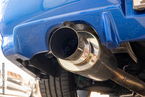 Low angle close up view of a polished stainless steel cannon exhaust muffler and tailpipe tip on a blue tuned car.