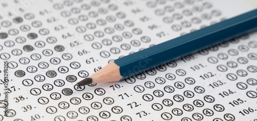 Blue pencil rests beside a test sheet. Darkened circles mark answers on exam paper. Question numbers line the page in orderly rows. Focal point emphasizes concentration and decision