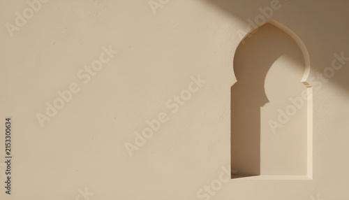 Minimalist beige stucco wall background featuring a traditional recessed moorish arch niche with soft sunlight and shadows