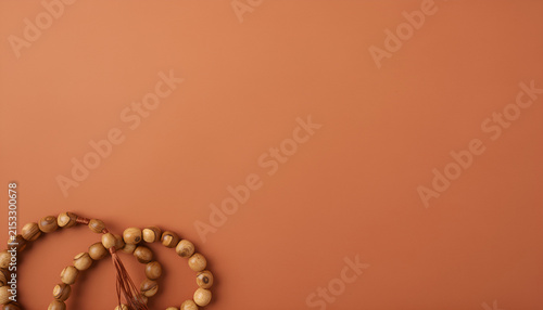 Top down flat lay of traditional wooden islamic prayer beads on a warm terracotta background with empty copy space