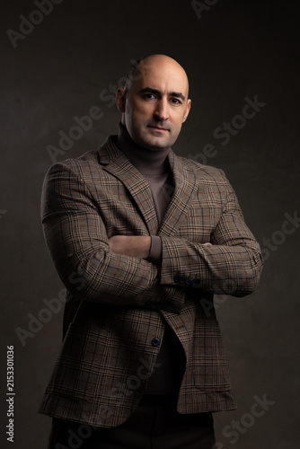 Serious middle aged man in blazer jacket with arms crossed in studio portrait