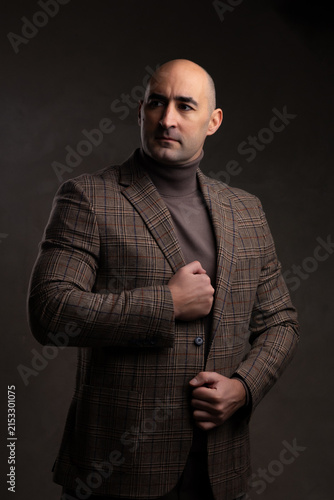 Serious middle aged Caucasian man in stylish blazer jacket in studio portrait with dark background