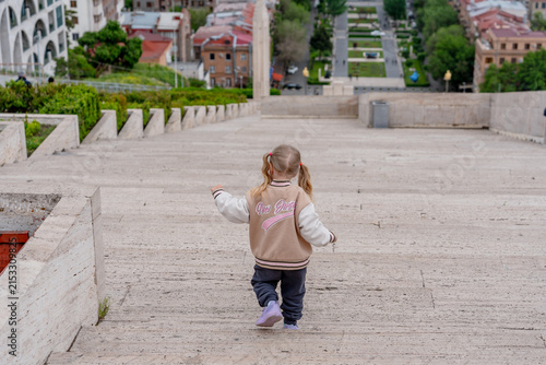 A sweet little child girl is running up the stairs on the street near the cascade in Armenia.