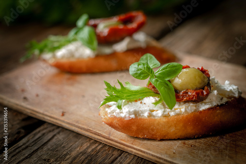 Bruschetta or crostini with cream cheese, sun-dried tomatoes, olives and fresh herbs. Tasty healthy snacks for breakfast