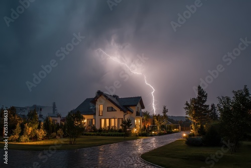 Lightning strikes near a modern house during a nighttime thunderstorm. Use it for weather reports or illustrating preparedness or home insurance.