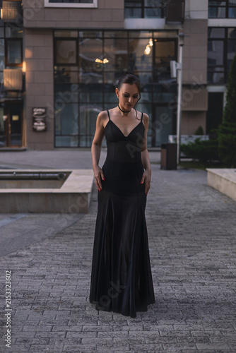 A beautiful woman in a luxurious black dress poses in the city