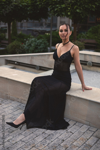 A beautiful woman in a luxurious black dress poses in the city
