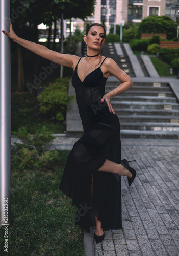 A beautiful woman in a luxurious black dress poses in the city