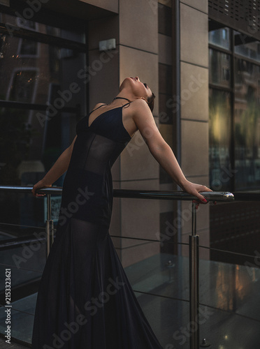 A beautiful woman in a luxurious black dress poses in the city