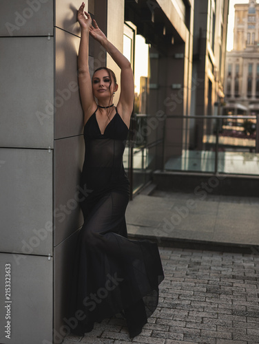 A beautiful woman in a luxurious black dress poses in the city