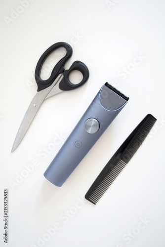 Flat lay composition of hair grooming essentials featuring a cordless electric trimmer, black hair comb, and stainless steel scissors neatly arranged on a clean white background.