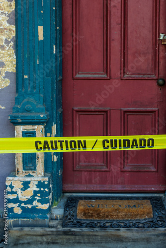 Caution tape covers a door with peeling paint and a welcome mat