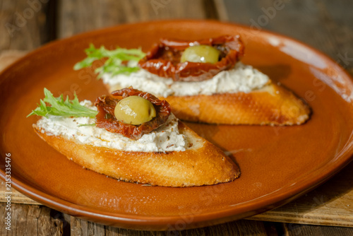 Crostini with cream cheese, sun-dried tomatoes, olives, fresh basil leaves and lettuce. Tasty healthy snacks.
