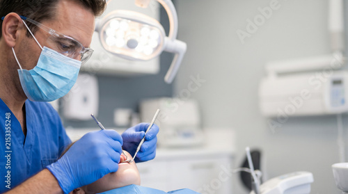 Dental Examination: A focused dentist, wearing protective gear, performs a dental examination on a patient in a modern clinic. The scene highlights professional healthcare and oral hygiene practices.