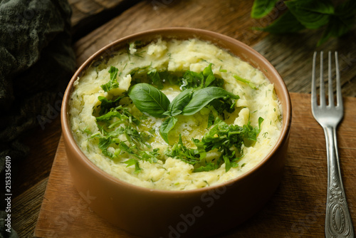 Bowl of mashed potatoes garnished with fresh herbs on rustic wooden table. Thanksgiving meal.