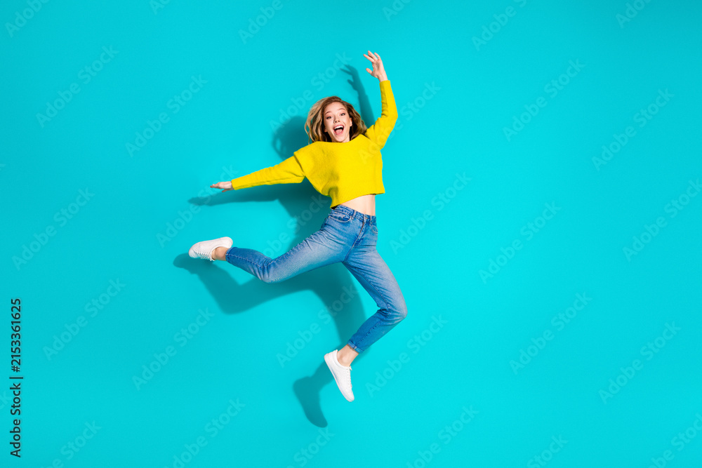 Fototapeta premium Joyful young woman jumps in a bright yellow sweater against a blue background for a vibrant fashion lifestyle stock photo