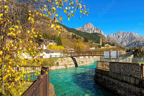 Alpine village of Pietraporzio in Piedmont, Italy, with a turquoise river, mountains and autumnal foliage.