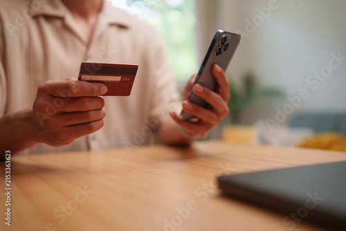 фотографія Man holding a payment card and smartphone at home for online registration and identity verification, representing secure authentication, mobile banking, digital payment and personal data