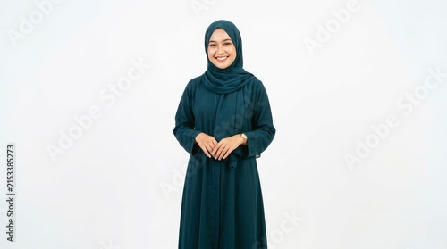 Smiling young woman wearing elegant dark blue hijab and modest traditional dress standing isolated on white background