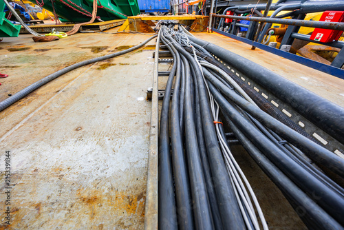 Bundle of heavy industrial electrical power cables laid in metal tray on rusty steel deck of vessel or offshore platform