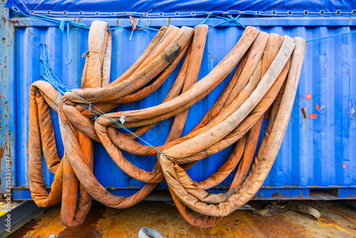 Heavy duty orange textile lifting slings hanging on blue corrugated cargo container wall at industrial site or shipyard