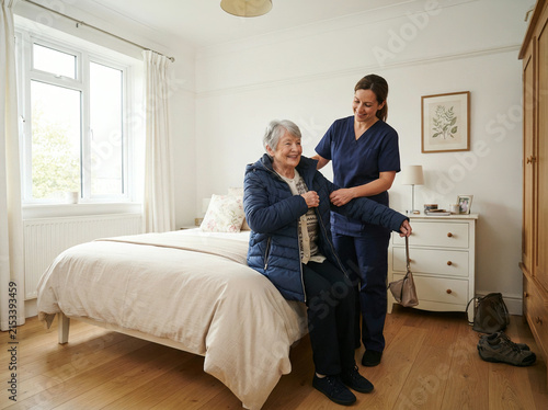 Care worker helping an elderly woman dress while seated on a bedroom bed