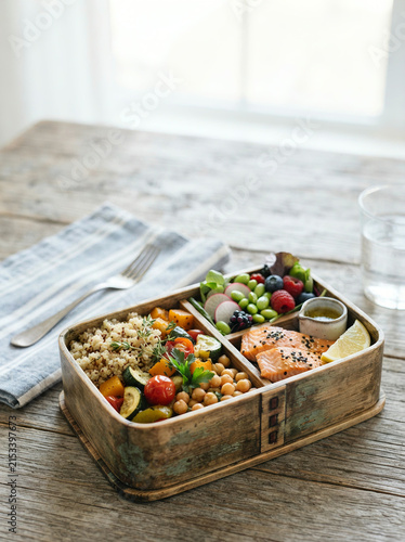 Wooden bento box filled with salmon, quinoa, roasted vegetables, and berries on a table