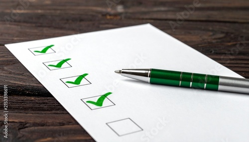 Close-Up of Checklist Paper with Green Checkmarks and Pen Resting on Dark Wooden Surface for Task Completion Concept