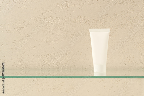 Blank White Cosmetic Tube on Glass Shelf Against Travertine Wall Background