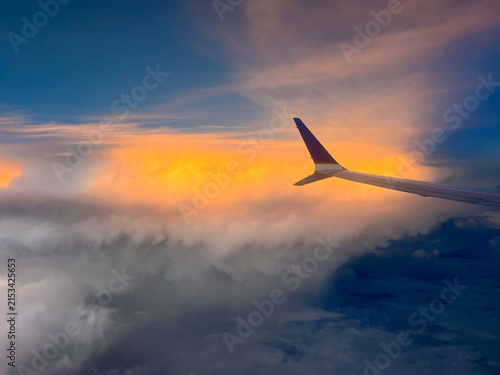Commercial airliner wing floating above soft clouds at sunset